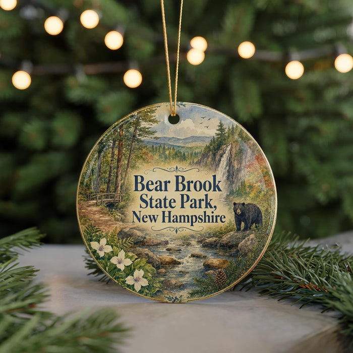 A round ornament featuring a scenic landscape with a bear, trees, and a stream, hanging from a string.