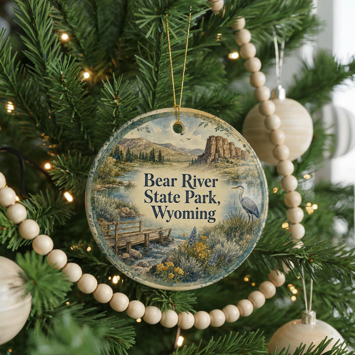 A round ornament hanging on a Christmas tree, featuring a scenic landscape with a bridge and mountains.