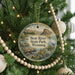 A round ornament hanging on a Christmas tree, featuring a scenic landscape with a bridge and mountains.