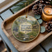 A decorative ornament featuring a scenic landscape of Beartown State Park, West Virginia, with pine cones, a candle, and greenery surrounding it.