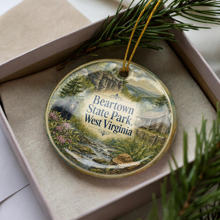 A decorative ornament with a scenic image of Beartown State Park West Virginia, featuring a river, mountains, and a cabin, is displayed in a box with pine branches.