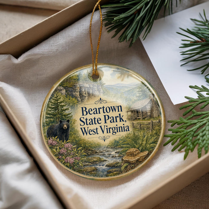 A decorative ornament with a bear standing in a forest, surrounded by pine trees and a stream, is displayed in a box.