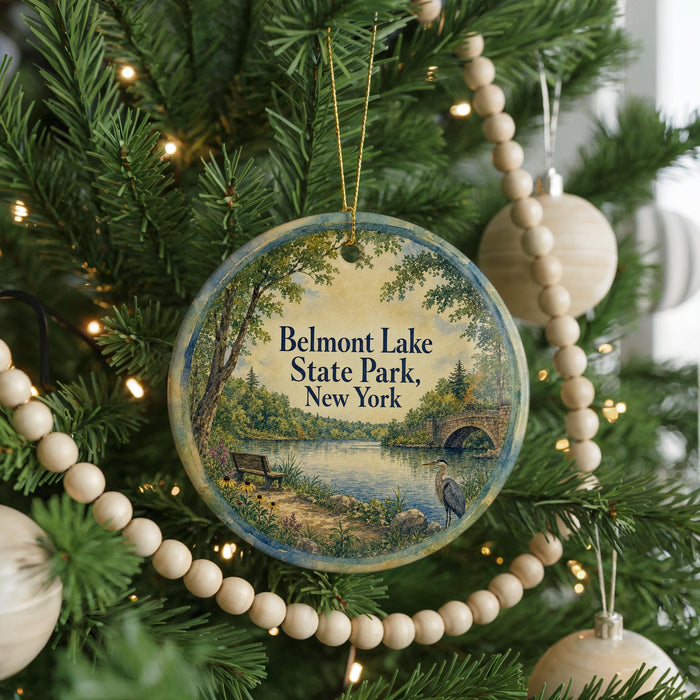 A round ornament hanging on a Christmas tree, featuring a scenic landscape with a lake, trees, and a bridge.
