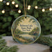 A round ornament with a painting of Belmont Lake State Park, New York, featuring a bench, a bird, and a bridge.