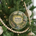 A round ornament hanging on a Christmas tree, featuring a scenic landscape with a bridge and a bird.