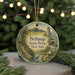 A round ornament with a painting of a park scene, featuring a bridge, trees, and a bird, hanging from a string.