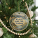 A round ornament hanging on a Christmas tree, featuring a scenic landscape with mountains, a lake, and a cabin.
