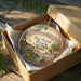 A decorative ornament in a box, featuring a scenic landscape with mountains, cacti, and a horse, with the text "Big Bend Ranch State Park, Texas" printed on it.