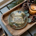 A decorative ornament featuring a scenic landscape of Big Pocono State Park, Pennsylvania, with pine cones, a candle, and greenery surrounding it.