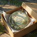 A decorative ornament in a box, featuring a scenic landscape with a waterfall and flowers, with the text "Big Ridge State Park, Tennessee" printed on it.