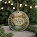 A round ornament with a painting of a scenic landscape, featuring a waterfall and a house, is displayed in front of a blurred background with Christmas lights.
