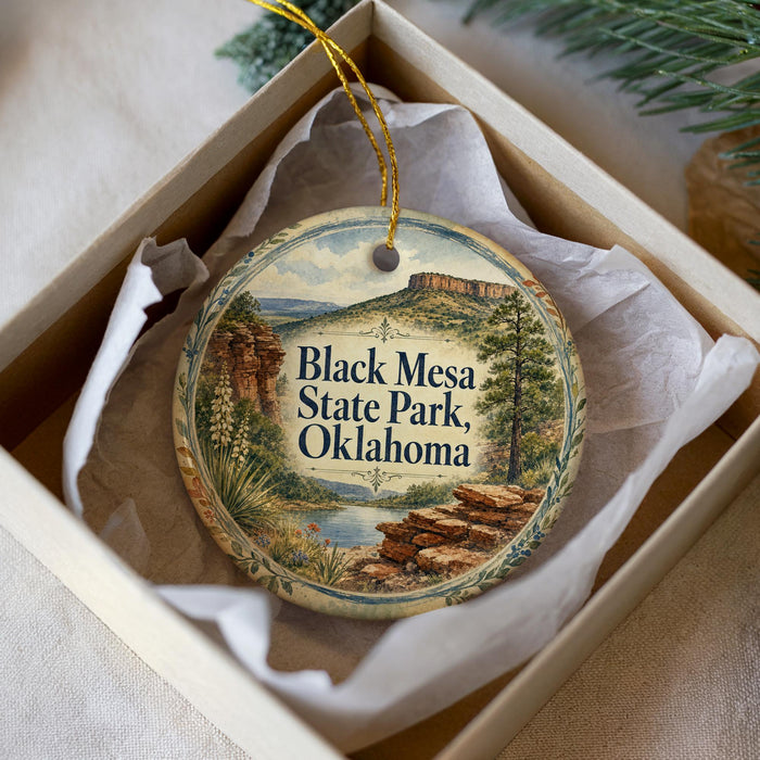 A decorative ornament in a box, featuring a scenic landscape with mountains, trees, and a river.