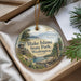 A decorative ornament with a scenic image of a park, featuring a lake, mountains, and a wooden structure, hanging from a string.