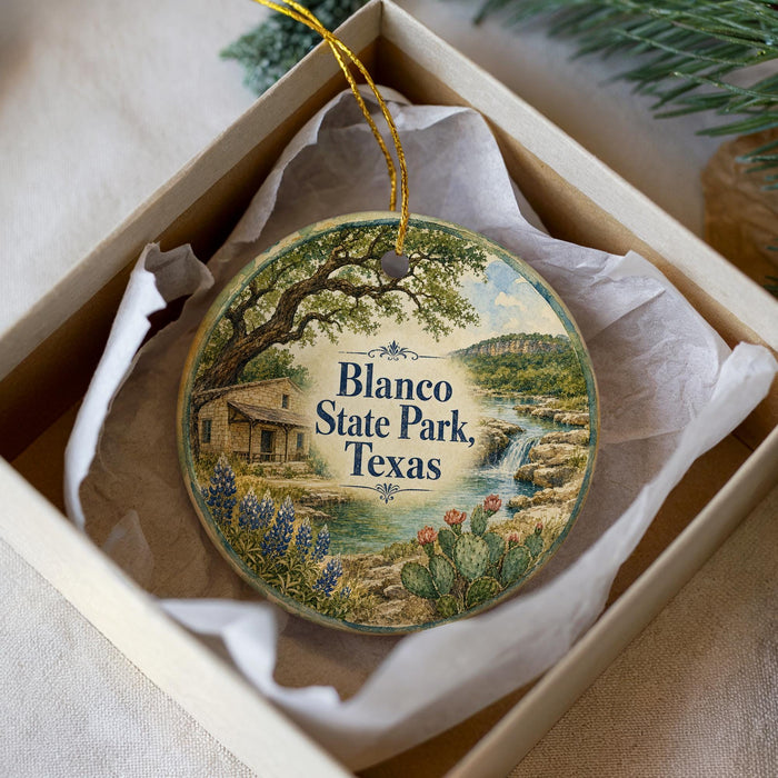 A decorative ornament in a box, featuring a scenic landscape with a house, trees, and a waterfall.
