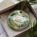 A decorative ornament with the text "Bledsoe Creek State Park, Tennessee" on it, placed in a box with pine branches.