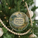 A circular ornament hanging on a Christmas tree, featuring a scenic landscape with a mountain and a river.