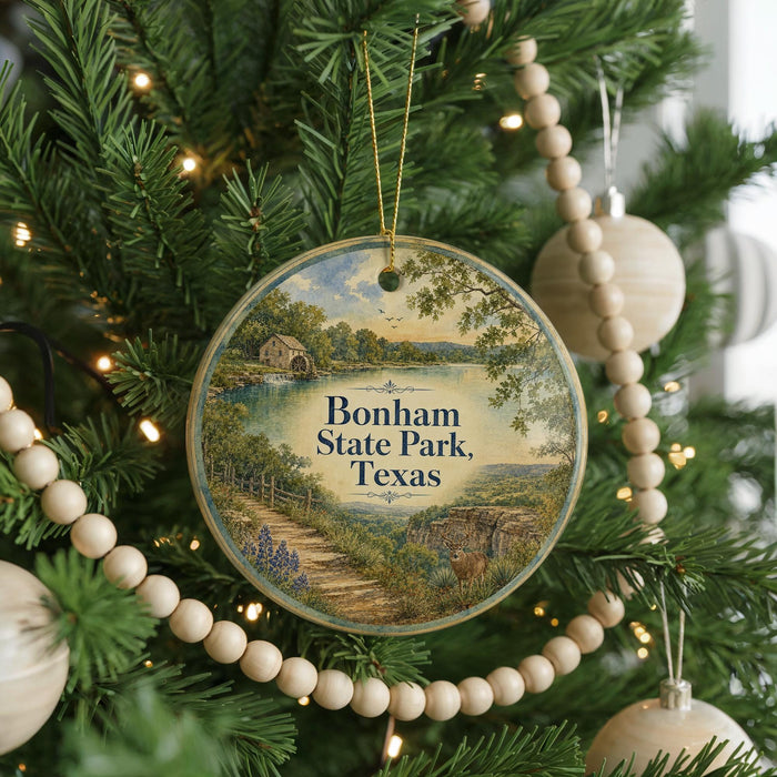 A round ornament hanging on a Christmas tree, featuring a scenic landscape with a path leading to a house and a lake.