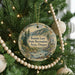 A round ornament hanging on a Christmas tree, featuring a scenic landscape with a river and mountains.
