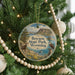 A round ornament hanging on a Christmas tree, featuring a scenic landscape with mountains, a lake, and wildlife.