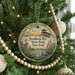 A round ornament hanging on a Christmas tree, featuring a bird and a pond scene with a bridge in the background.