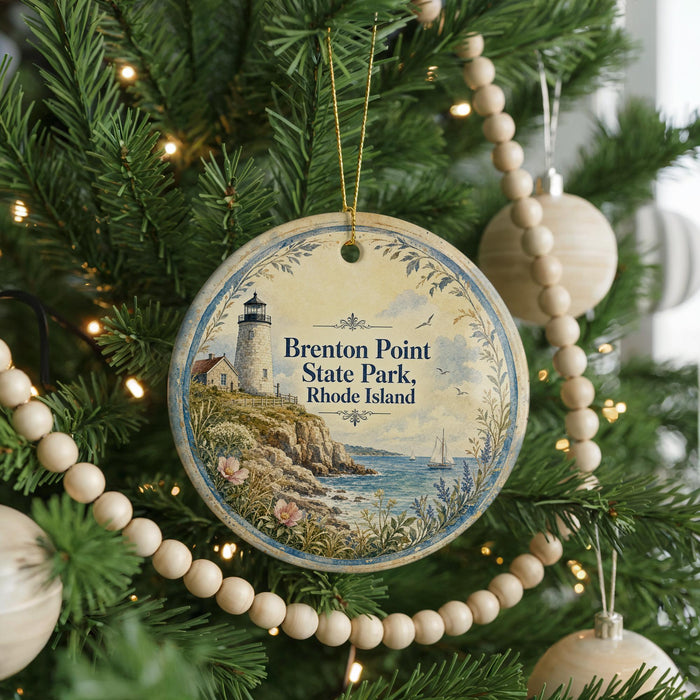A round ornament hanging on a Christmas tree, featuring a lighthouse and a coastal scene.