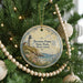 A round ornament hanging on a Christmas tree, featuring a lighthouse and a coastal scene.