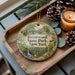 A round ornament with the text "Brentwood State Park, New York" on it, surrounded by pine cones and a lit candle on a wooden tray.