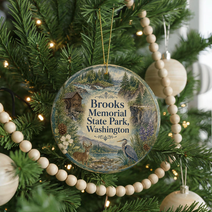 A round ornament hanging on a Christmas tree, featuring a scenic landscape with a cabin, trees, and wildlife.