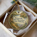 A decorative ornament in a box, featuring a scenic landscape with a river, trees, and a bird.