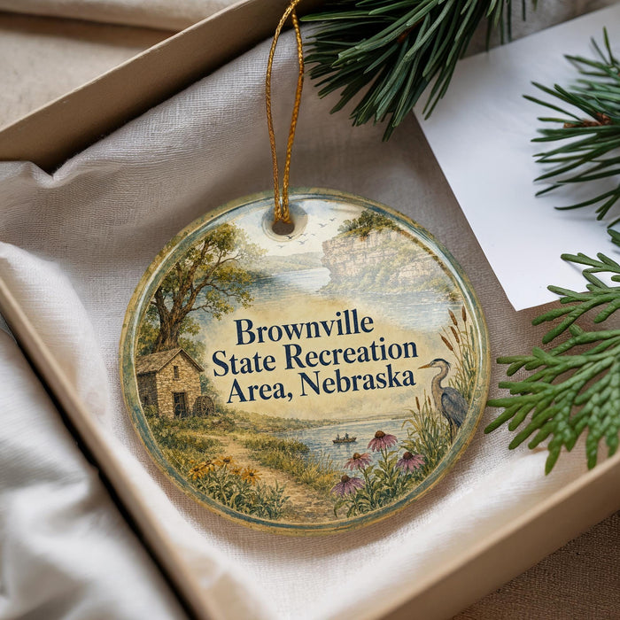 A decorative ornament with a scenic landscape and text, placed in a box with pine branches.