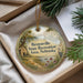 A decorative ornament with a scenic landscape and text, placed in a box with pine branches.