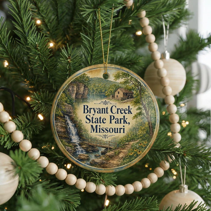 A round ornament hanging on a Christmas tree, featuring a scenic image of a waterfall and a house, with the text "Bryant Creek State Park, Missouri" displayed on it.