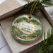 A decorative ornament in a box, featuring a scenic landscape with a lake, trees, and a bird, along with the text "Buckhorn State Park, Wisconsin".