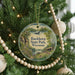 A round ornament hanging on a Christmas tree, featuring a scenic landscape with a lake and mountains.
