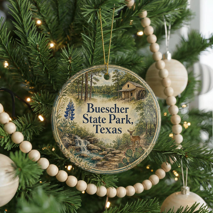 A round ornament on a Christmas tree, featuring a scenic image of Buescher State Park, Texas, with a deer and a waterfall.