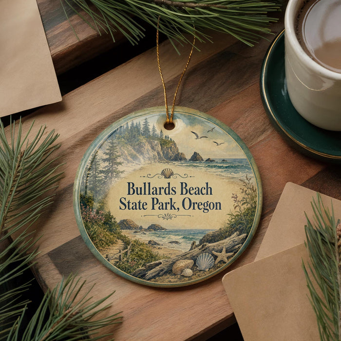 A decorative ornament with a scenic beach landscape, featuring a path leading to a rocky cliff, pine trees, and a body of water. The ornament is hanging from a string and is placed on a wooden surface, surrounded by pine branches and a cup of coffee.