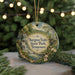 A round ornament with a scenic image of a waterfall and forest, surrounded by greenery, is displayed against a blurred background with twinkling lights.