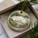 A decorative ornament in a box, featuring a scenic landscape with a river, bridge, and houses, with the text "Burlingame State Park, Rhode Island" printed on it.