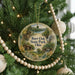 A round ornament hanging on a Christmas tree, featuring a scenic landscape with a cabin and a lake.