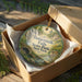 A round ornament in a box, featuring a scenic image of Buttermilk Falls State Park in New York.
