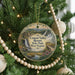 A round ornament hanging on a Christmas tree, featuring a scenic landscape with a waterfall and a cabin in the distance.