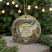 A round ornament with a scenic landscape of a waterfall, mountains, and a cabin, hanging on a string.