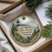 A decorative ornament with a lighthouse and a scenic view of Cape Meares State Scenic Viewpoint, Oregon, is displayed in a box with pine branches.