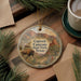 A decorative ornament featuring a scenic image of Caprock Canyon State Park, Texas, with a bison and desert landscape. The ornament is placed on a wooden surface, surrounded by pine branches and a cup of coffee.