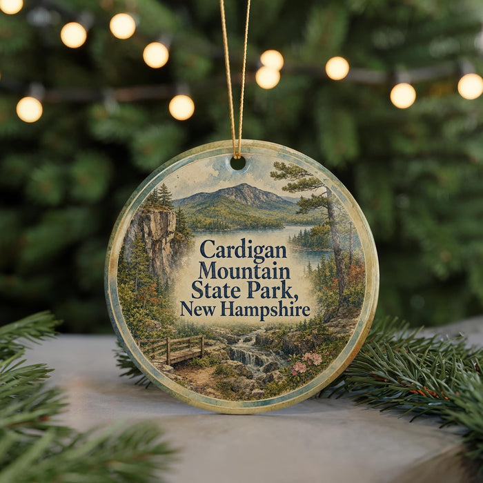 A circular ornament featuring a scenic landscape of Cardigan Mountain State Park, New Hampshire, with a mountain, lake, and forest in the background.