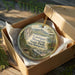 A wooden box containing a round ornament with a scenic mountain landscape and text that reads "Cardigan Mountain State Park, New Hampshire".