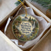 A decorative ornament in a white box, featuring a scenic landscape with a waterfall, cabin, and mountains.