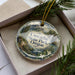 A decorative ornament with the text "Cascadia State Park, Oregon" on it, placed in a box with pine branches.