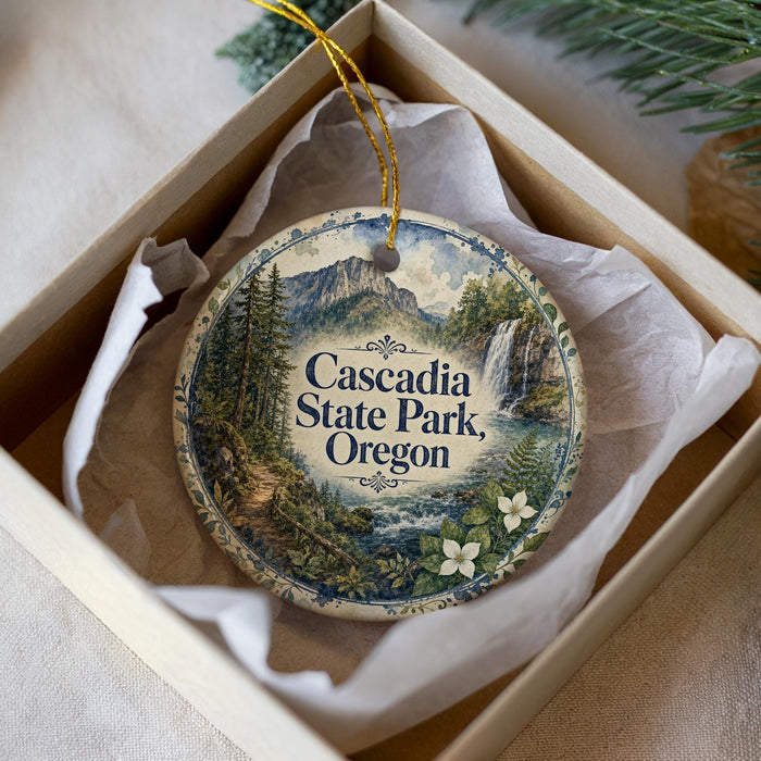 A decorative ornament in a box, featuring a scenic landscape with mountains, a waterfall, and a path leading through the forest.