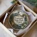 A decorative ornament in a box, featuring a scenic landscape with mountains, a waterfall, and a path leading through the forest.